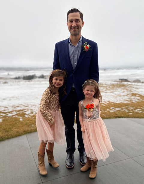 Greg and his two daughters outside with snow in the background.